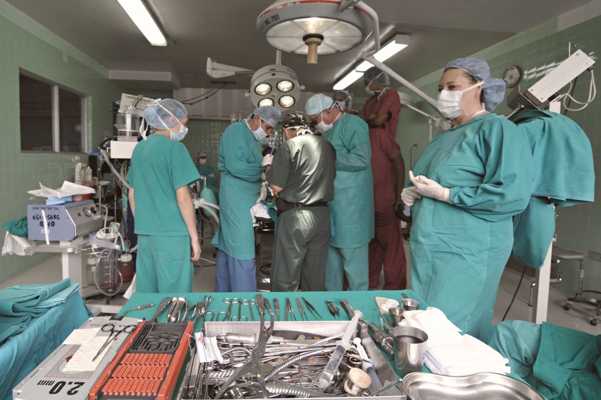 Equipe médica em centro cirúrgico durante procedimento, com instrumentais organizados sobre a mesa
